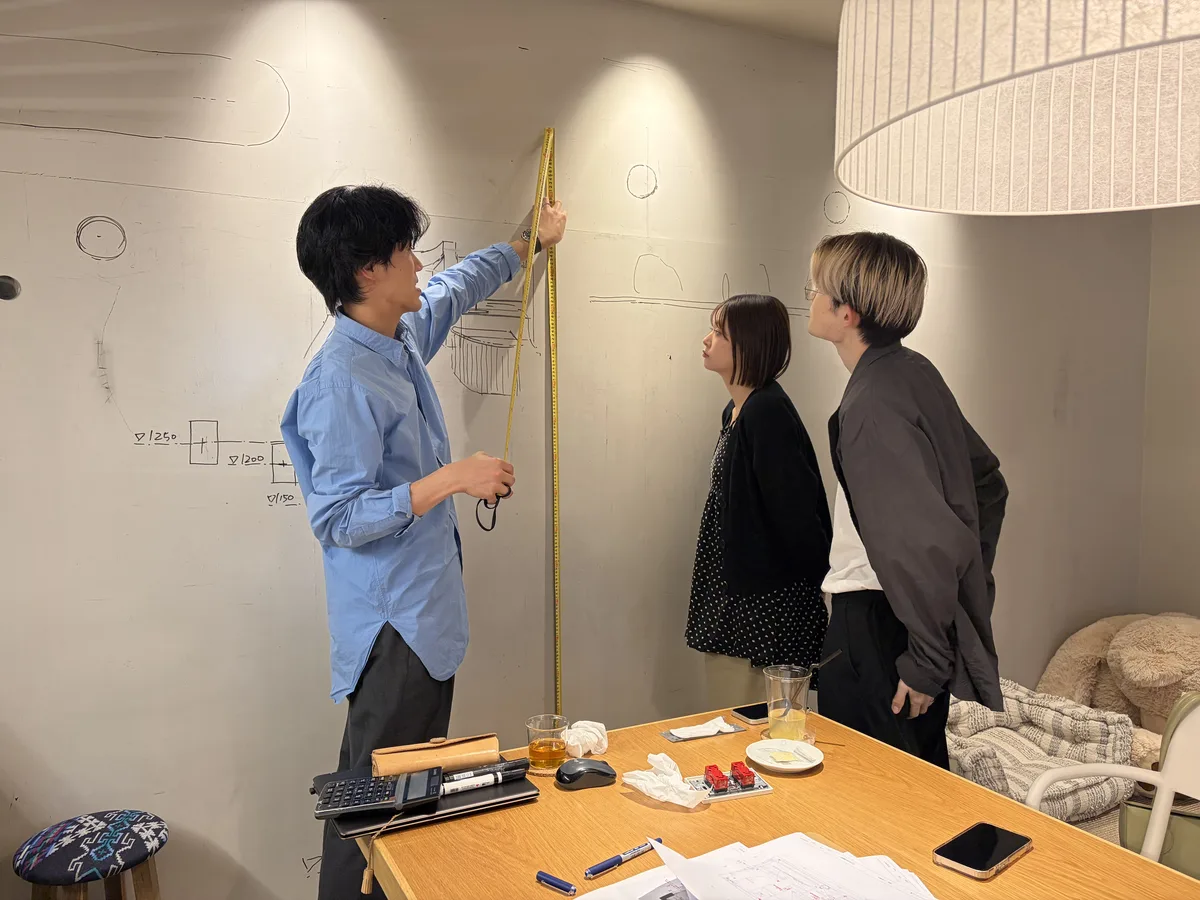 壁にメジャーを当てるスタッフと、それを見るご夫婦
