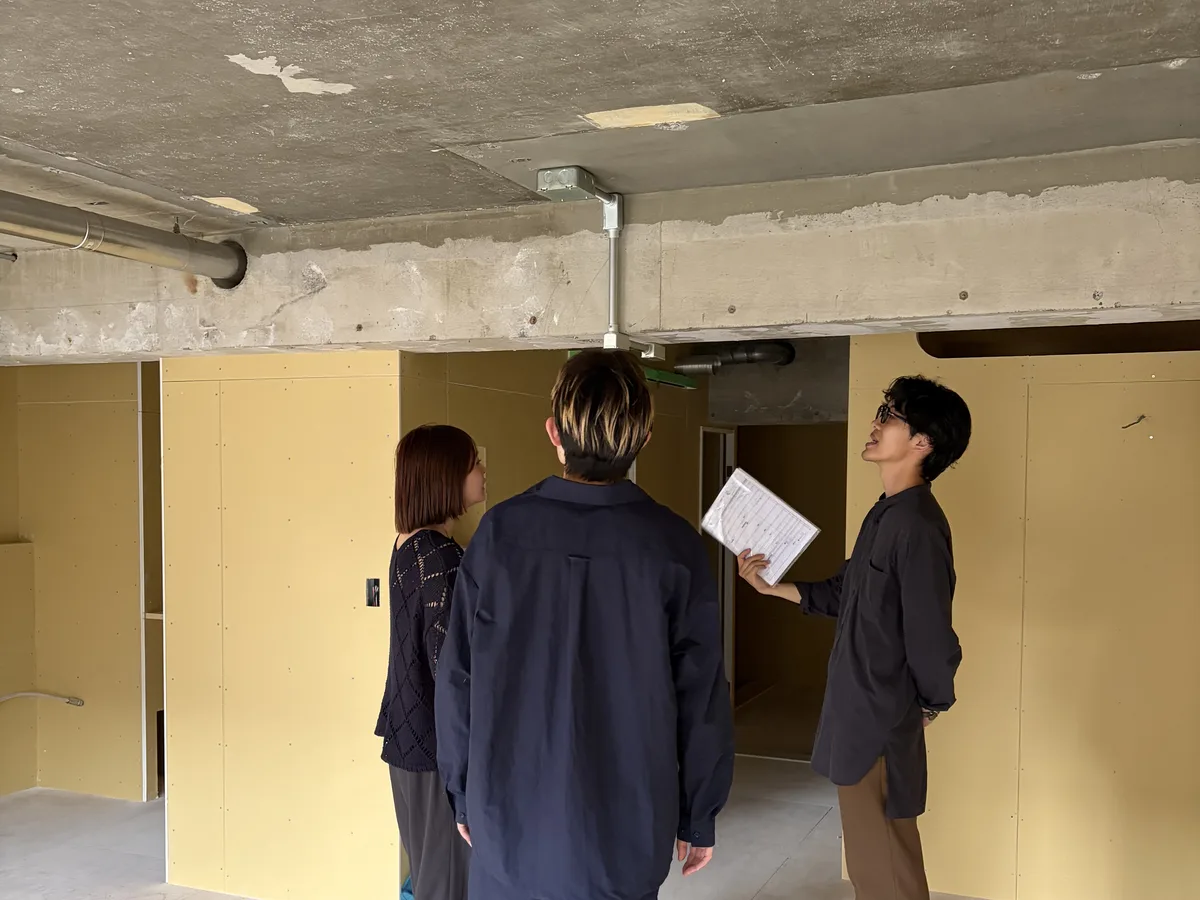工事中の室内で、資料を持つデザイナーと話すご夫婦